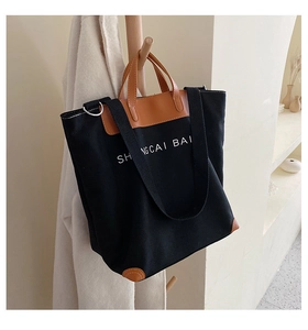 Detail of canvas tote bag with brown leather trim and white lettering on a wooden hanger