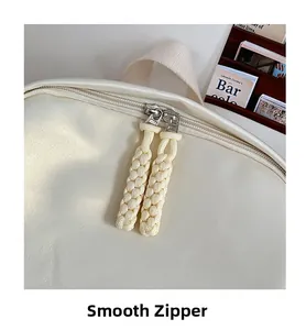 Close-up of smooth double zipper with woven pullers on a creamy white minimalist backpack