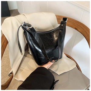 Close-up of black pleated glossy leather shoulder bag with silver zipper and wide strap