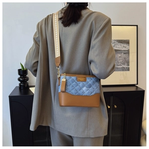 Detail of blue denim and brown leather bucket bag with quilted pattern and wide strap