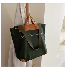 Detail of dark green canvas tote bag with brown leather stitching and white lettering