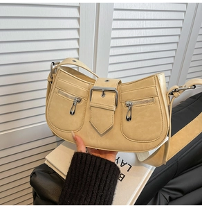 Detail of cream beige half-moon bag featuring symmetric zip pockets and buckle