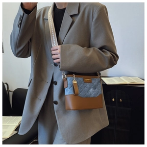 Detail of a quilted denim and brown leather bucket bag with a wide geometric shoulder strap