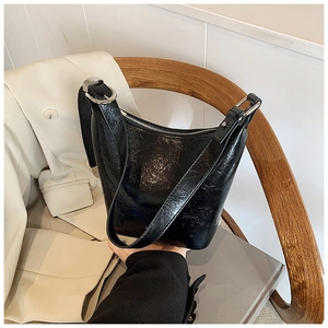 Close-up of black pleated patent leather bucket bag with silver hardware on a wooden chair