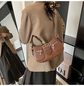 Detail of a dark brown half-moon underarm bag with silver buckles and zip pockets
