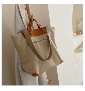 Detail of canvas tote bag with brown leather trim and shoulder strap on wooden rack