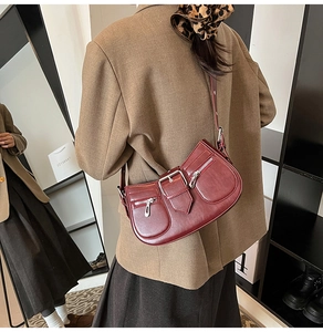 Detail of burgundy leather shoulder bag featuring metallic buckle and zipper pockets