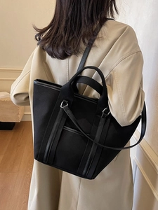 Large black canvas tote bag worn by a model in a beige trench coat for a casual look