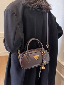 Classic dark brown leather Boston bag with gold hardware shown on a black wool coat
