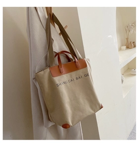 Detail of canvas tote bag featuring contrast leather trim and printed logo lettering