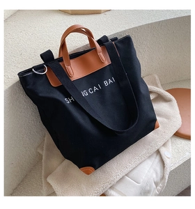 Black canvas tote bag with brown leather trim resting on a white fleece jacket