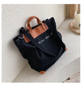 Detail view of large black canvas tote bag featuring brown leather trim and white typography