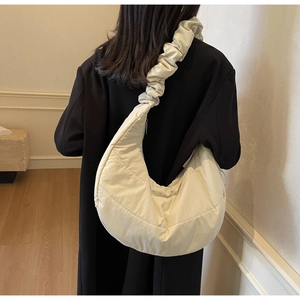 Detail of a beige quilted nylon hobo bag with ruffled cloud strap on a black coat