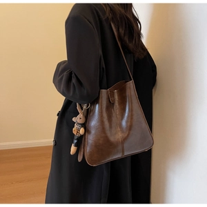 Detail of dark brown leather bucket bag featuring a cute plush bunny charm and long strap
