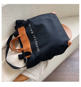 Detail of black canvas tote bag showing brown leather handles and reinforced corner patches