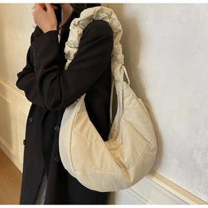 Quilted cream hobo bag with adjustable ruched shoulder strap shown on a dark coat