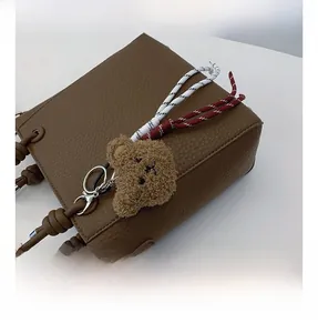 Detail of brown litchi pattern leather bucket bag with teddy bear charm and braided rope