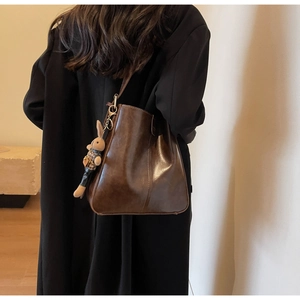Detail view of deep brown leather tote bag with a cute rabbit doll charm on the strap