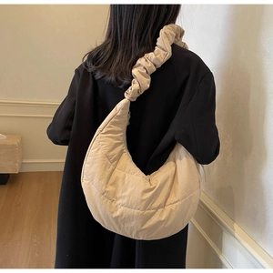 Detail of beige quilted nylon crescent bag featuring a stylish ruffled shoulder strap