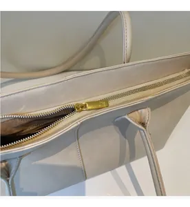 Detailed close-up of smooth gold metal zipper closure on beige tote bag
