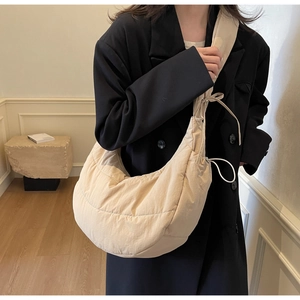 Detailed view of beige quilted crescent nylon shoulder bag on model in minimalist room
