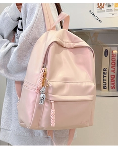 Detail of pink backpack with woven rope zipper pulls and a silver bear keychain charm