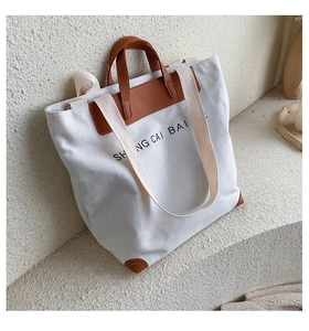 Detail of canvas tote bag showing brown leather handles and stitched corner protectors