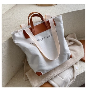 Detail of canvas tote bag showing brown leather stitching and black printed letters