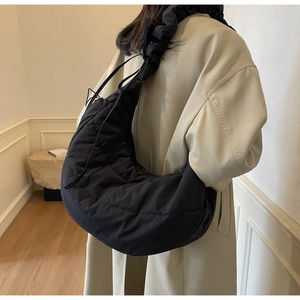 Close-up of black quilted puffer hobo bag with pleated handle on a beige coat model