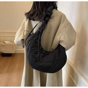 Side view of a black quilted nylon crescent bag with ruffled strap worn by a model