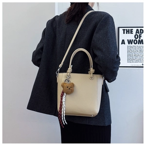Back view of a beige lychee leather bucket bag with a cute bear charm and crossbody strap