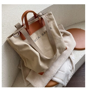 Detail of canvas tote bag with brown leather trim and metal ring for shoulder strap