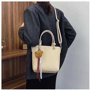 Detail view of beige lychee leather bucket bag with cute brown bear charm and metal feet