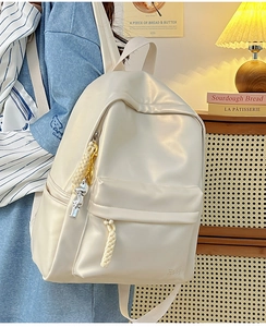 Model wearing a cream minimalist faux leather backpack with decorative silver pendant