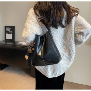 Detail view of large black leather bucket bag with a cute bear charm on an ivory sweater