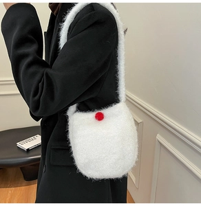 Detail of white plush bucket bag with soft faux fur texture and a red pompom accent