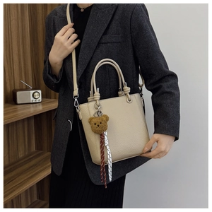 Close-up of beige lychee texture bucket bag with bear charm on a dark grey blazer model