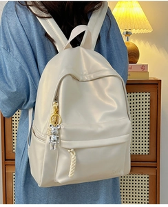 Detail of minimalist beige backpack with front zipper pocket and silver bear keychain