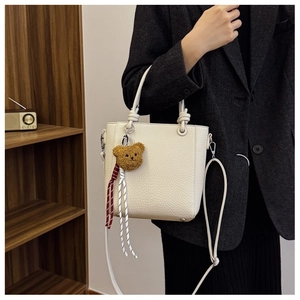 Detail of off-white lychee pattern leather tote with knot handle and bear charm