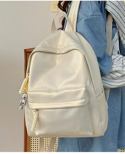 Detail view of cream leather backpack with woven zipper pulls and a robot charm