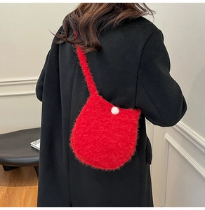 Detail of red plush bucket bag featuring soft faux fur texture and a white pompom charm