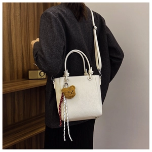Detail of cream lychee texture leather tote bag with cute brown teddy bear charm