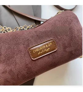Dettaglio della borsa a cilindro in camoscio rosso-marrone con catena floreale dorata e hardware