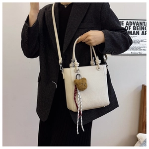 Detail view of cream lychee leather bucket bag with cute bear charm and silver hardware