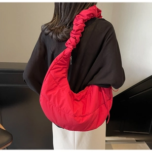 Detail of red quilted half-moon bag with ruffled shoulder strap worn by a model
