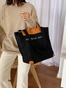 Black canvas tote bag with brown leather trim and shoulder strap shown on a model