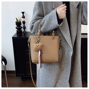 Detail of khaki pebbled leather bucket bag with plush bear charm and striped ribbon