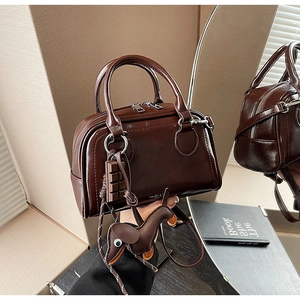 Detail einer braunen glänzenden Boston-Tasche mit Hundeanhänger und Schokoladen-Charm