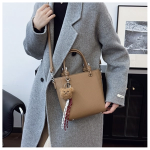 Detail of khaki leather bucket bag with top handles, crossbody strap, and cute bear charm