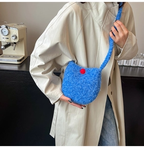 Blue fuzzy bucket bag with red pom-pom shown on model in a cozy indoor setting